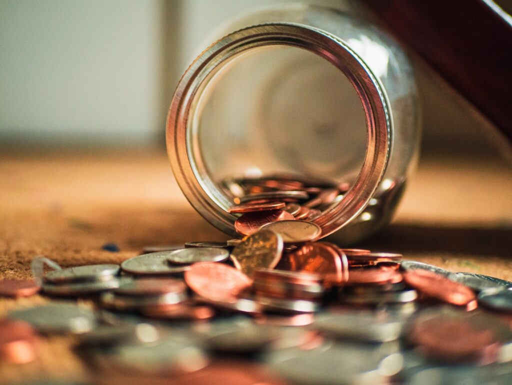 Assorted coins spilling out of a glass jar